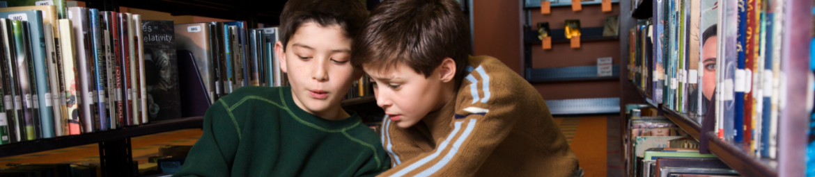 2 Jungen unterhalten sich zwischen Bücherregalen